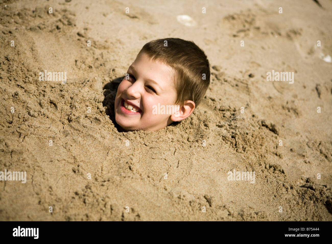 Boy, (7) buried up to his neck in the sand, Grand Beach Provincial Park, Manitoba, Canada Stock Photo