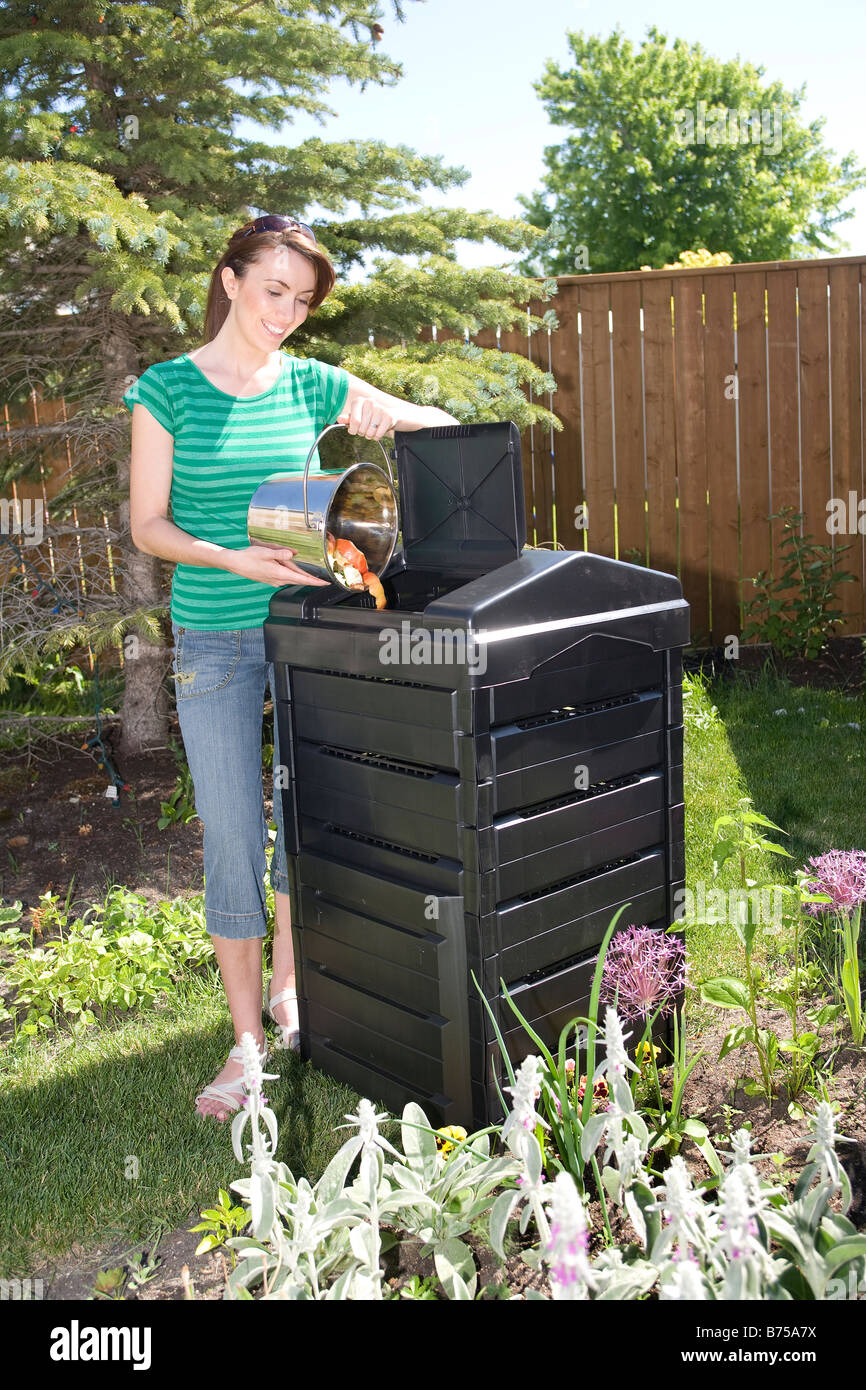 Woman With Compost Pail Beside Composter In Backyard Winnipeg Stock