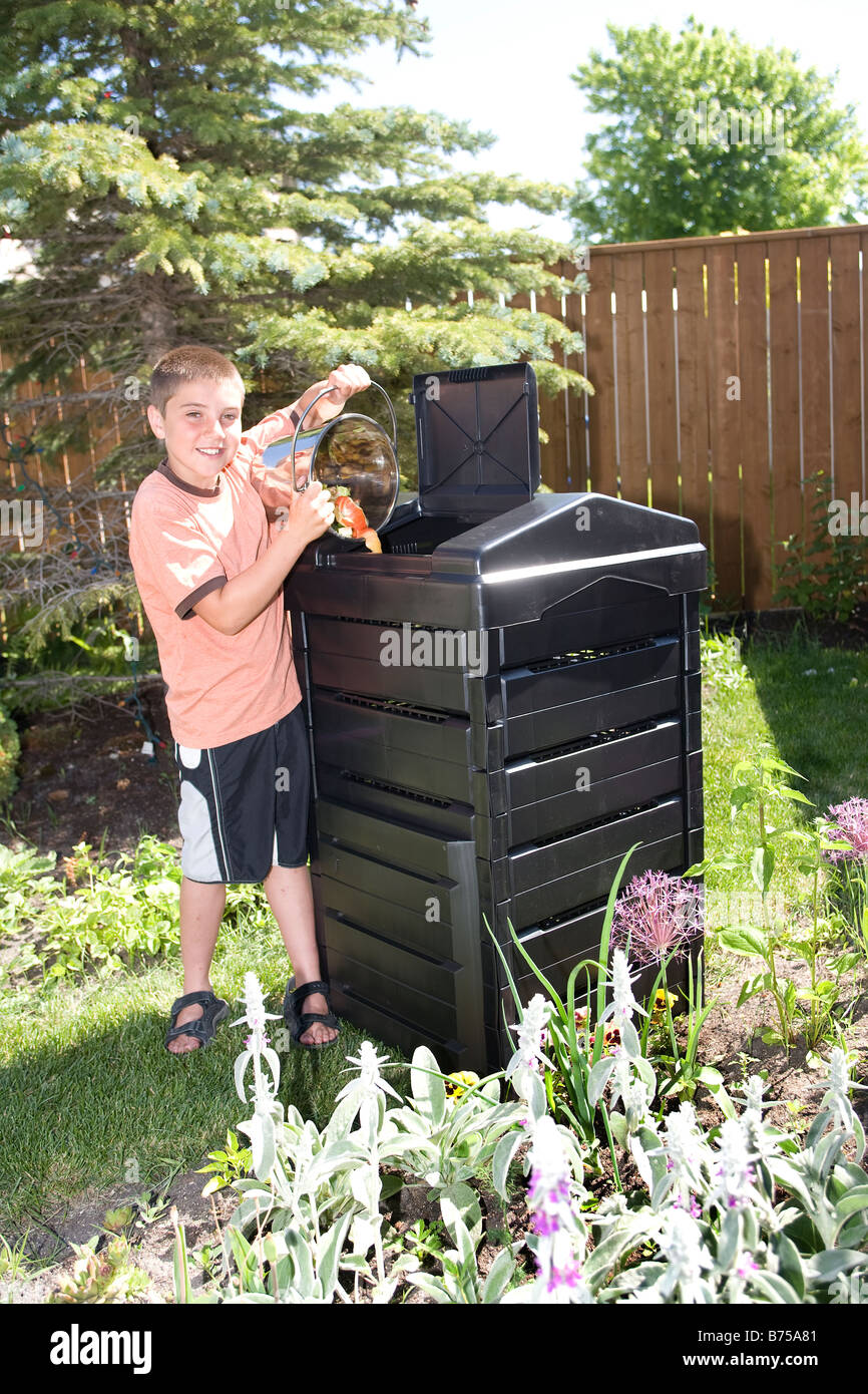 Boy with compost pail beside composter in backyard, Winnipeg, Manitoba, Canada Stock Photo