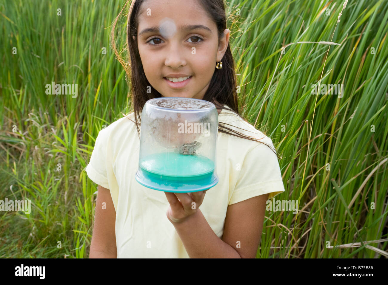 8 year old girl in wetland holding frog in collecting jar, Winnipeg, Canada Stock Photo