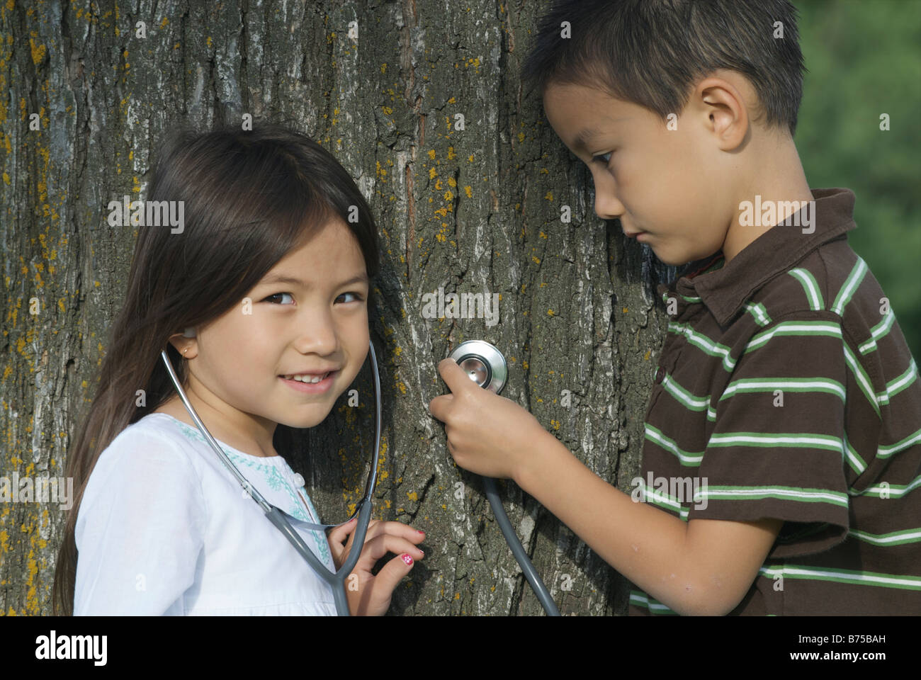 Five year old sister and seven year old brother with stethescope on tree, Winnipeg, Canada Stock Photo