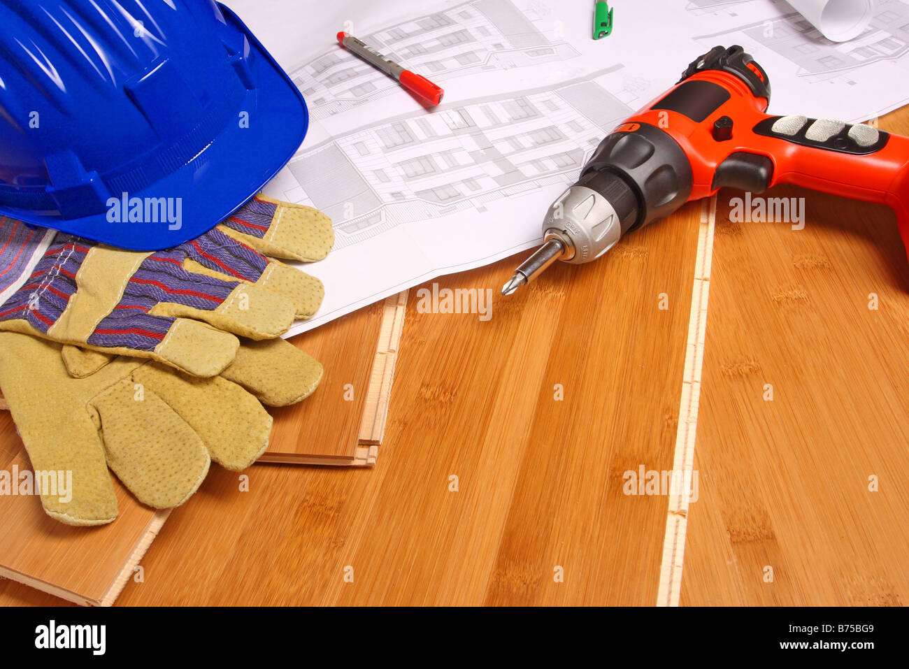 helmet gloves drill and blueprint on wood floor Stock Photo