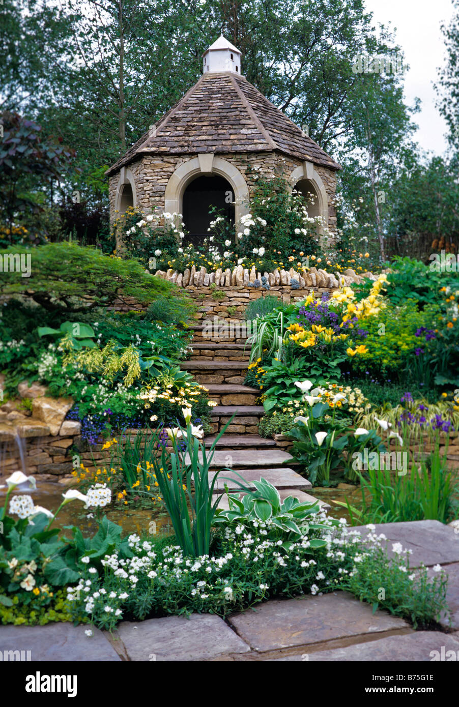 Flagstone steps over pool and mixed herbaceous planting leading to a Cotswold stone folly Stock Photo