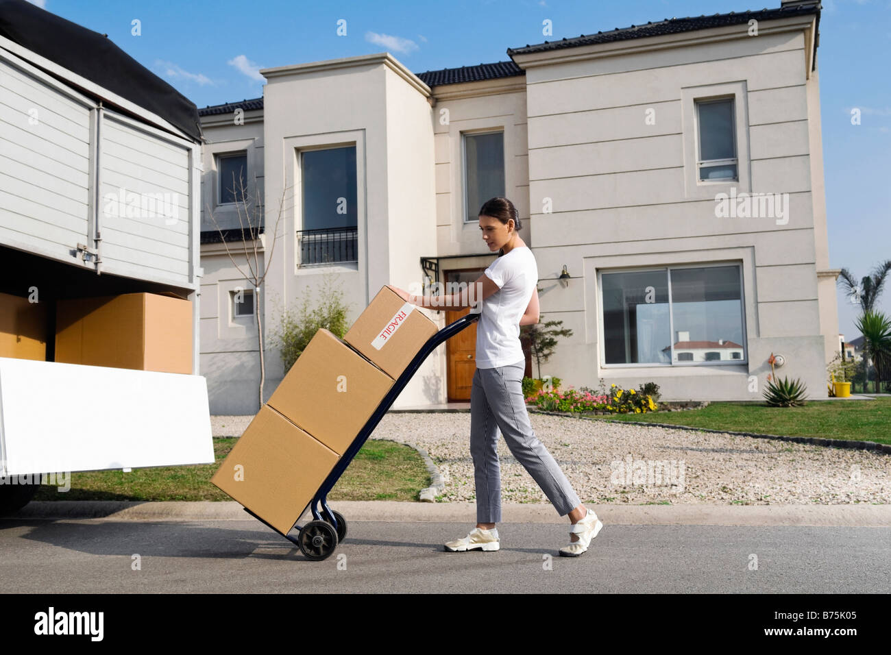 Side profile of a young woman pushing a push cart with cardboard boxes Stock Photo