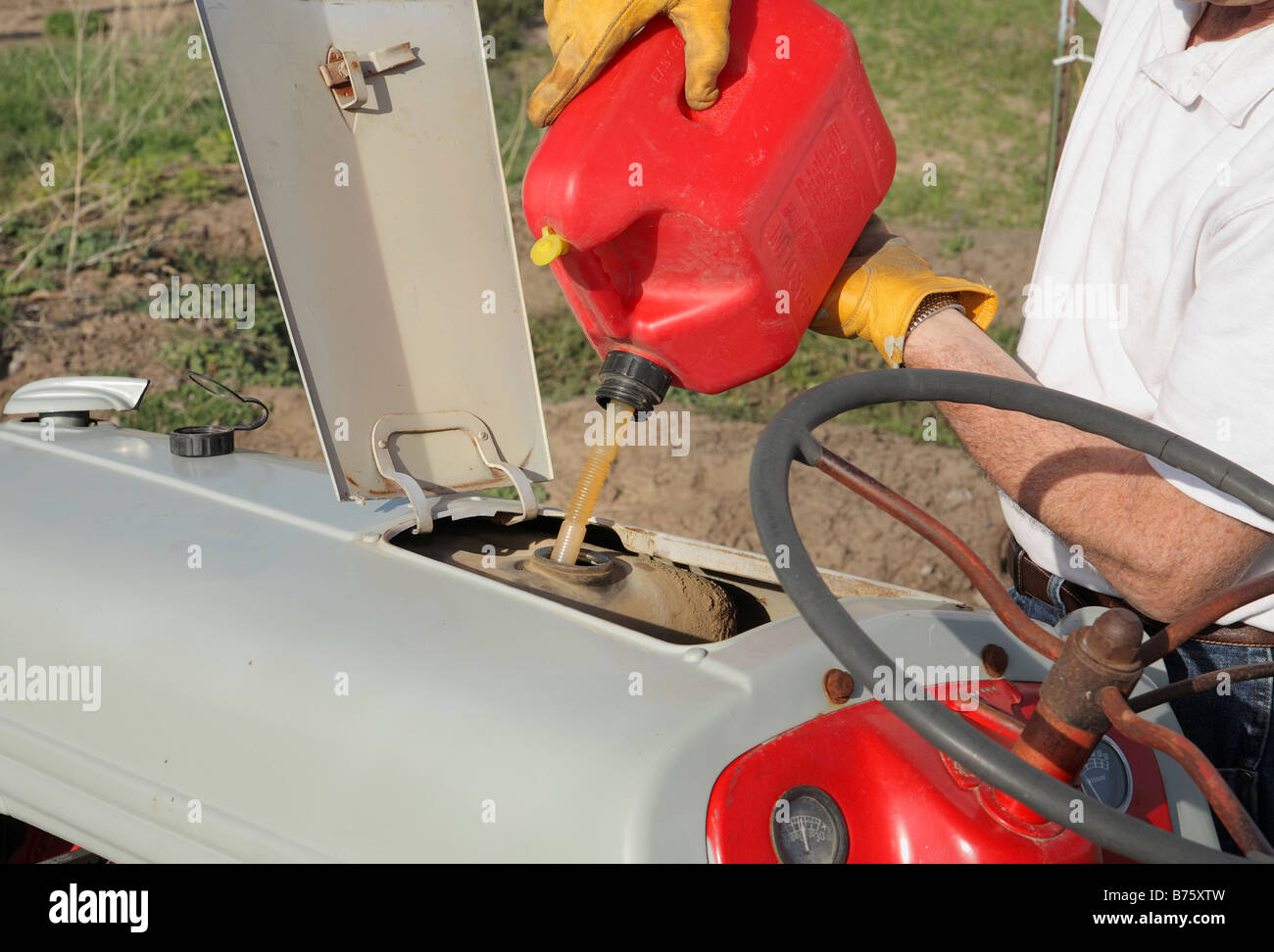 farmers hands refueling a tractor from red gas can Stock Photo