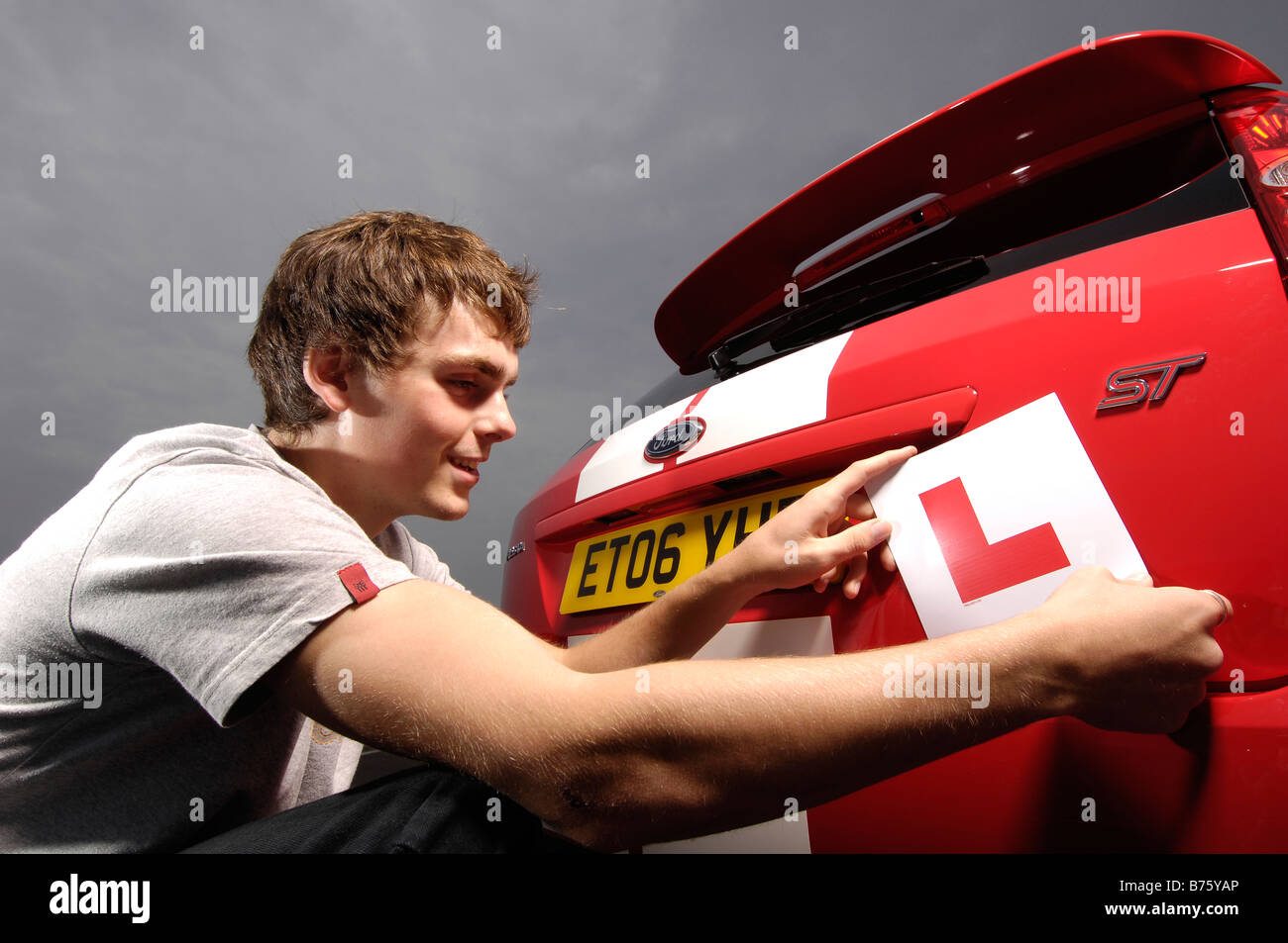 smiling student driver, puts L plates on red car Stock Photo