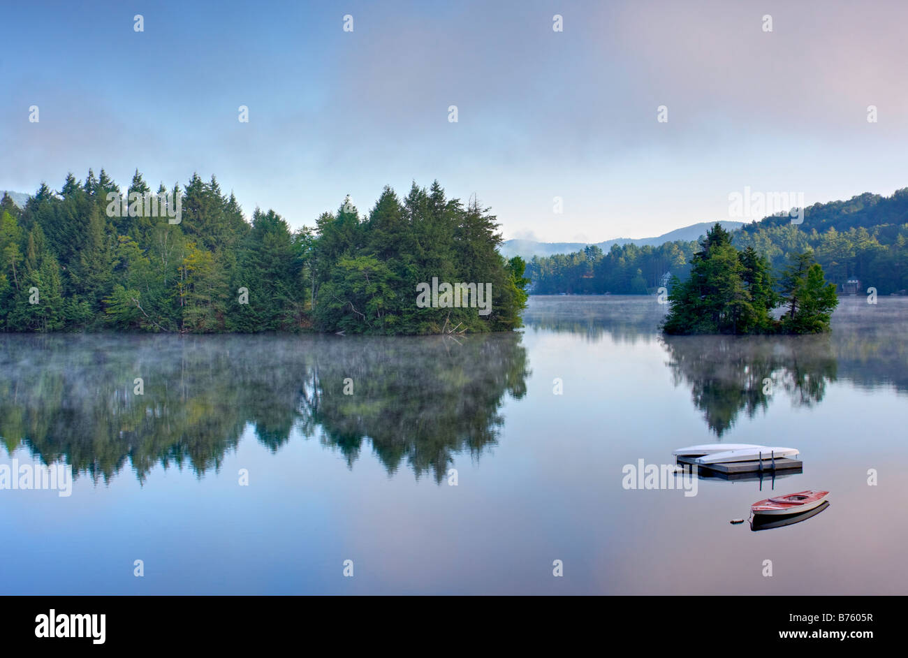 A lake in the early morning with fog on the water A boat and dock are ...