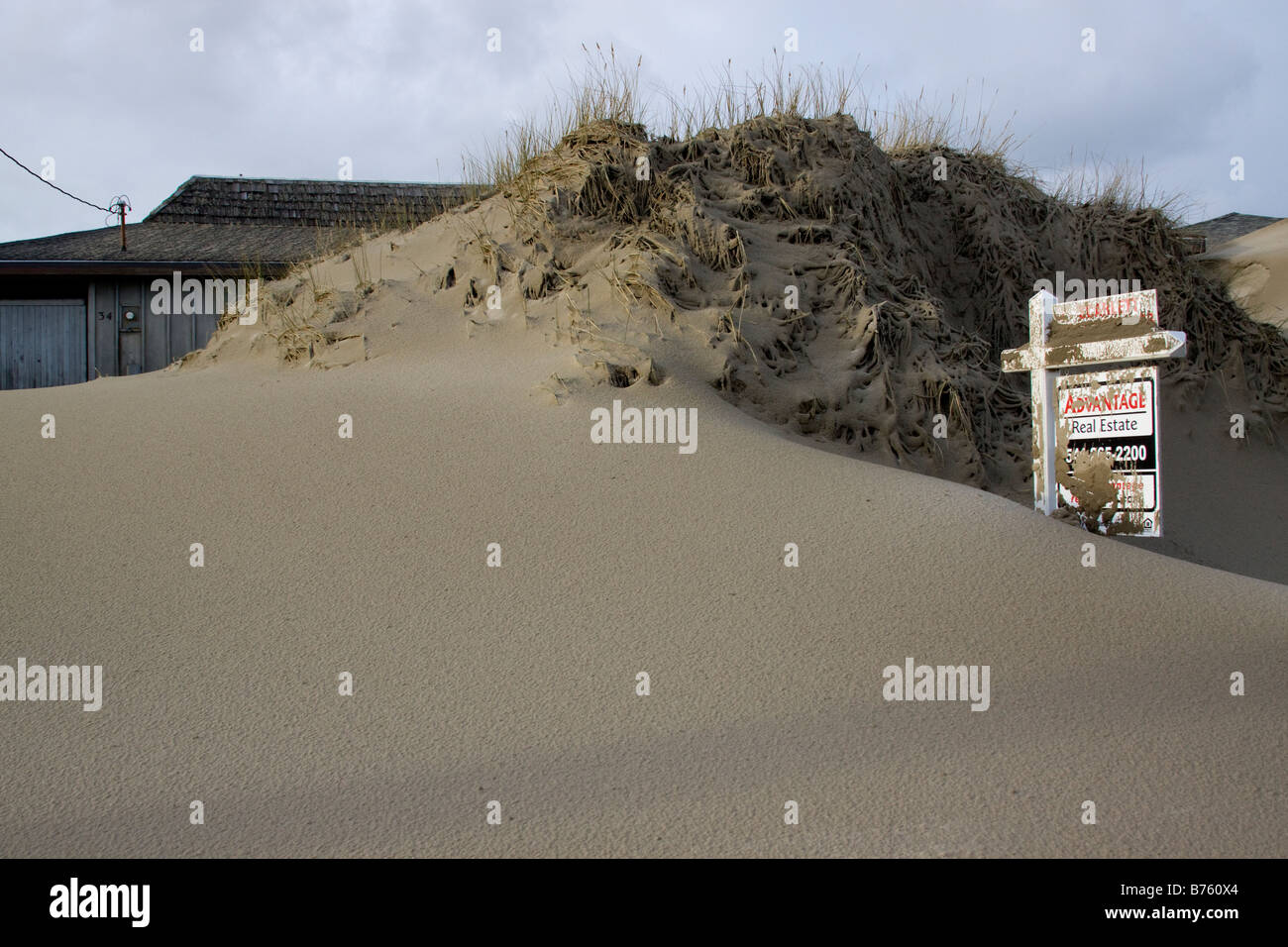 Sand dunes pile high against residences and a for sale sign after a winter storm on the Oregon coast. Stock Photo