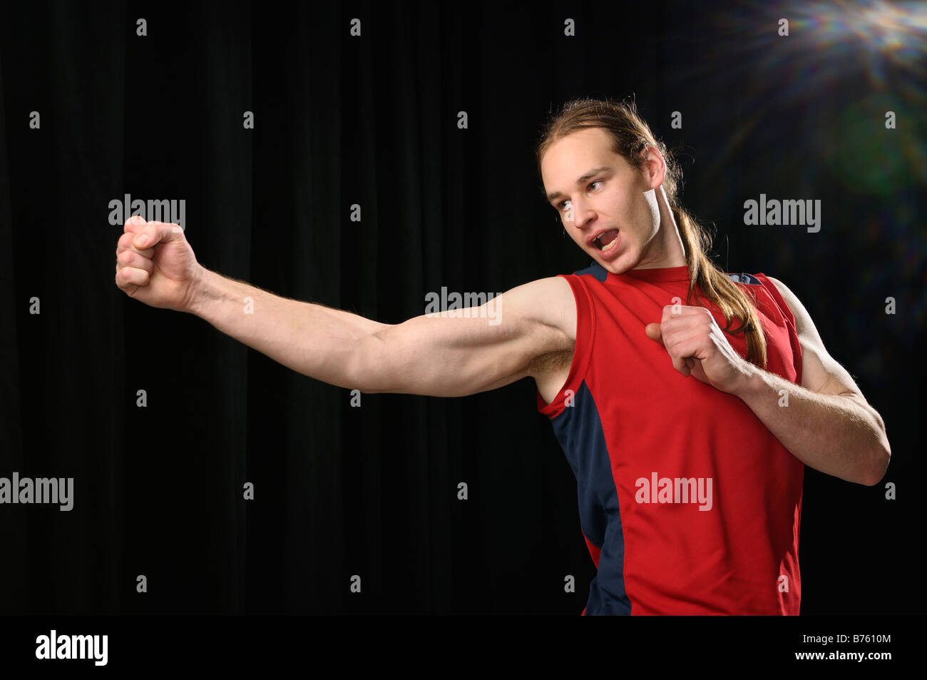 Young male with long hair practicing a swivel Karate punch while yelling in spotlight Stock Photo