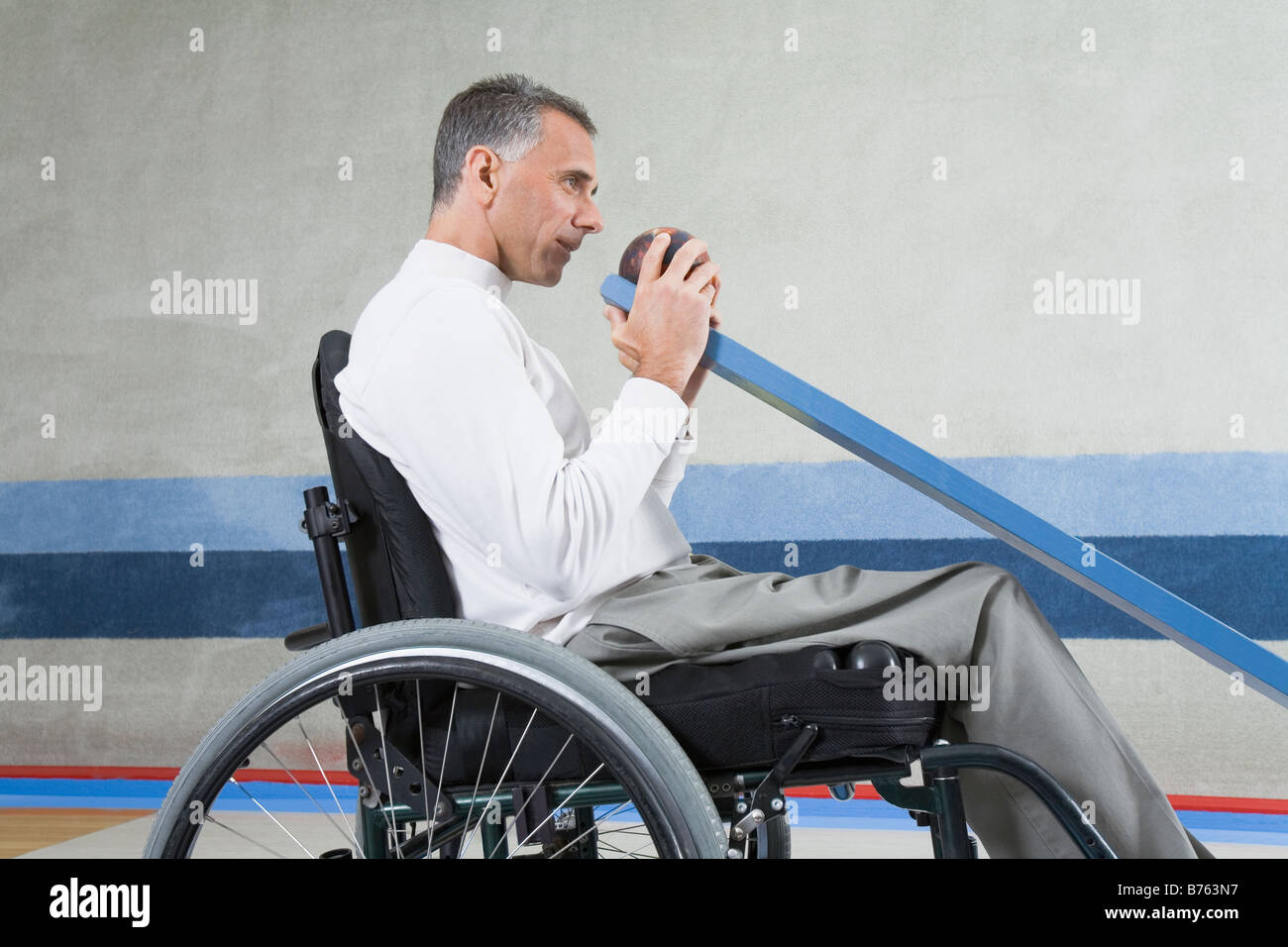 Side profile of a mature man sitting in a wheelchair and playing ten pin bowling Stock Photo