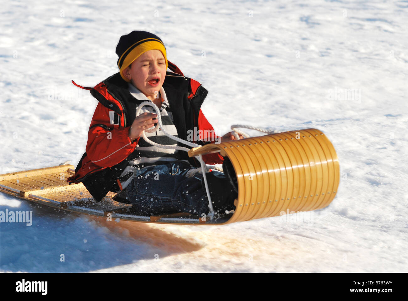 A young boy sledding down a snowy hillside in the mountains of Utah