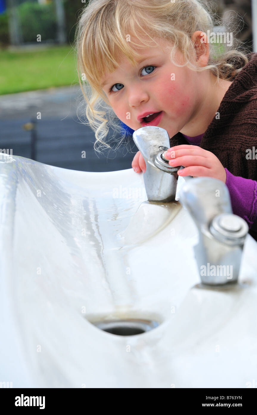 Cute school little girl drinks water from reusable pink bottle outdoor.  Child in hat enjoys fresh cold water on green summer street. Body  rehydration Stock Photo - Alamy