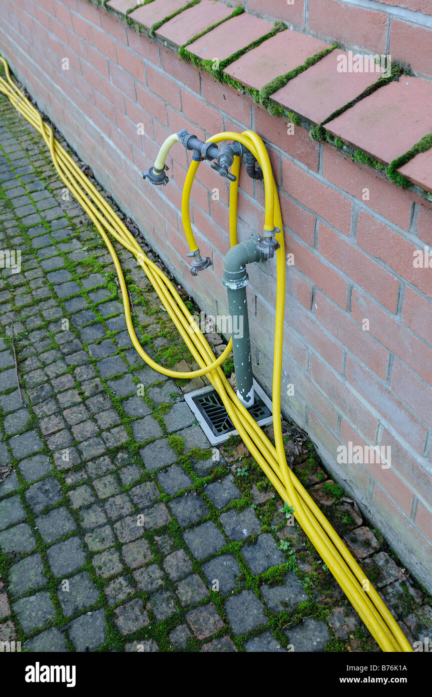 Garden hose tap outlet on house wall with yellow hosepipe Stock Photo