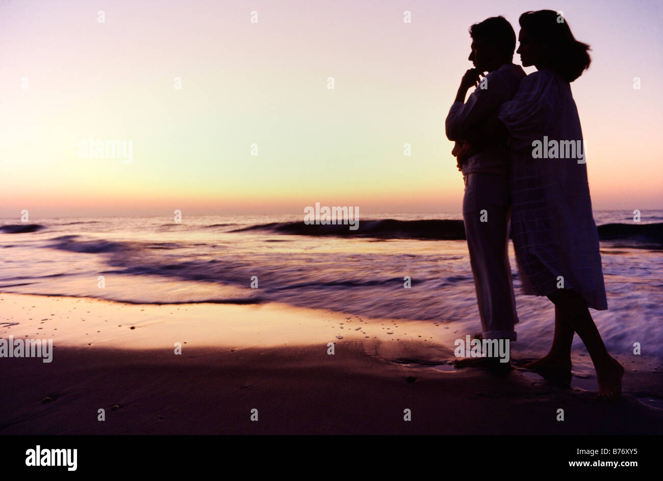 Couple watching sunrise at ocean's edge Stock Photo