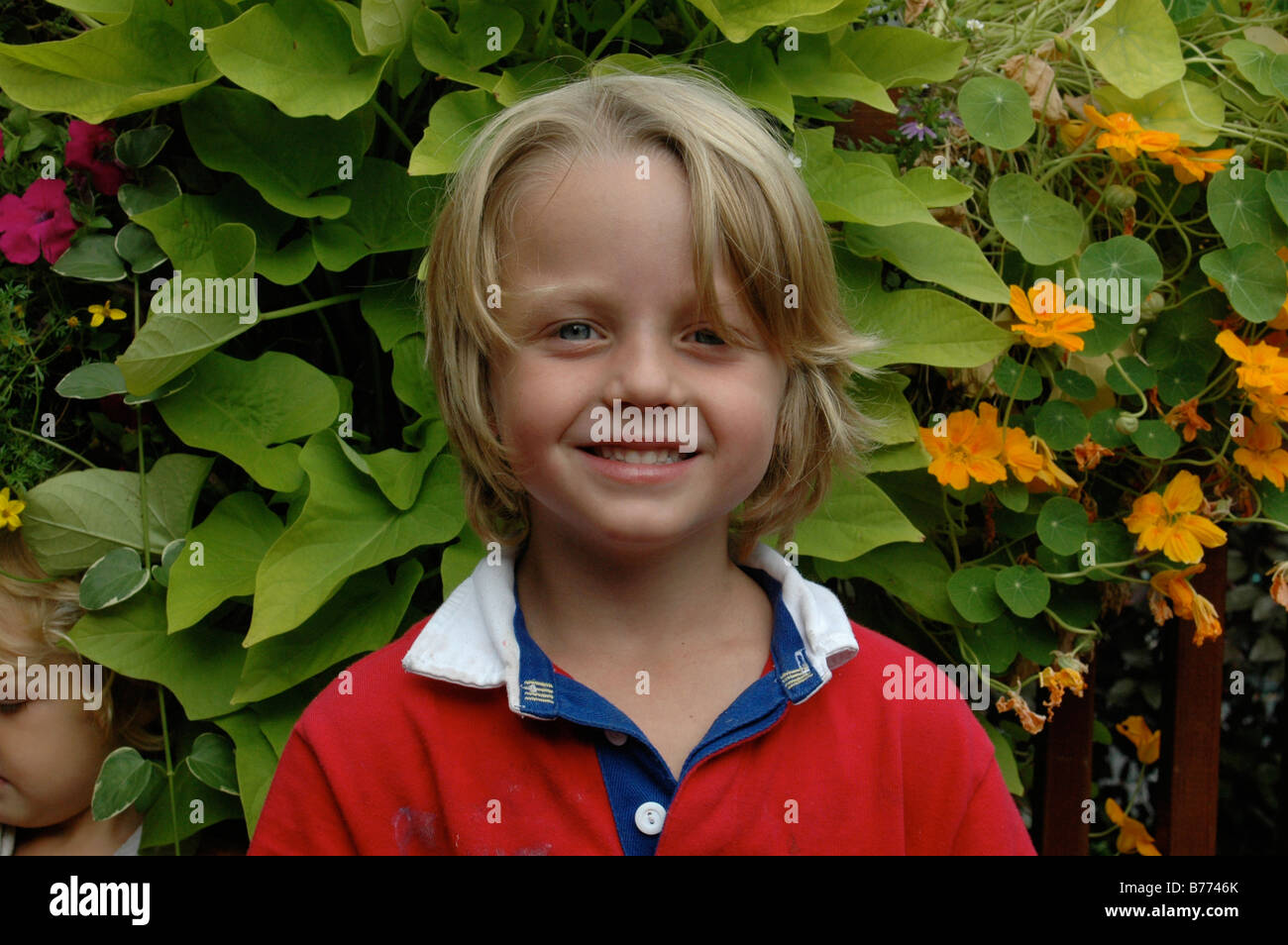 Beautiful young boy with a beaming smile posing in the garden, with his younger brother tucked in at his side. Stock Photo