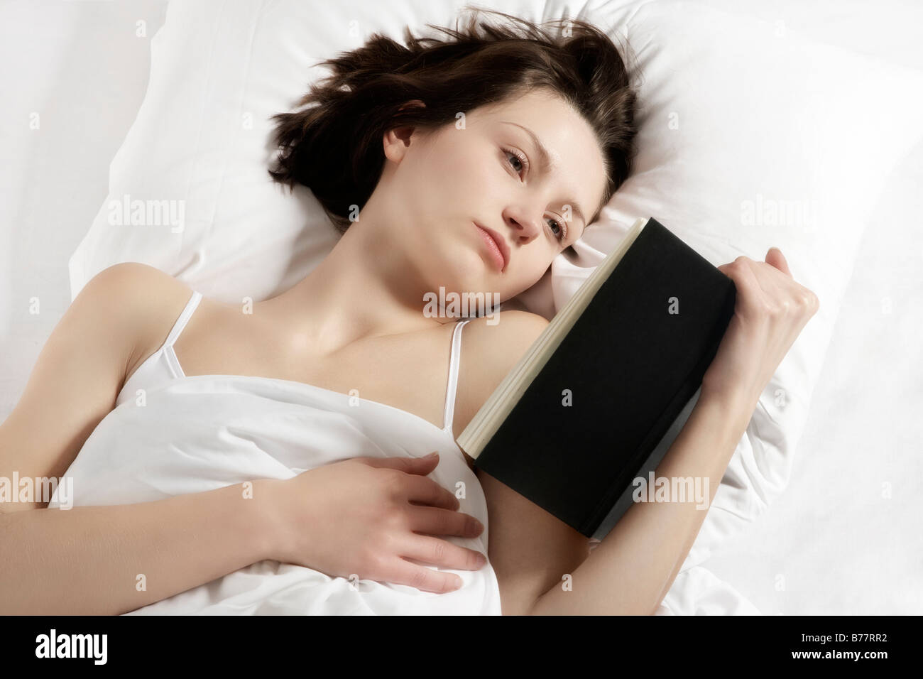 Young brunette woman reading a book in bed Stock Photo