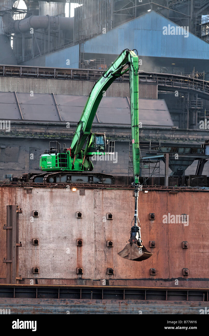 Modern mechanical digger, unloading in front of industrial setting, Krupp Mannesman smeltery, Rhine harbour, Duisburg, Ruhr are Stock Photo