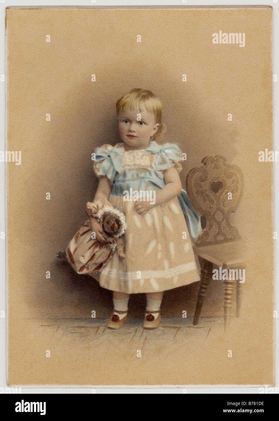 Original tinted portrait of cute Victorian child (girl or boy as they were dressed the same in these times) holding a doll, circa 1880's, U.K. Stock Photo
