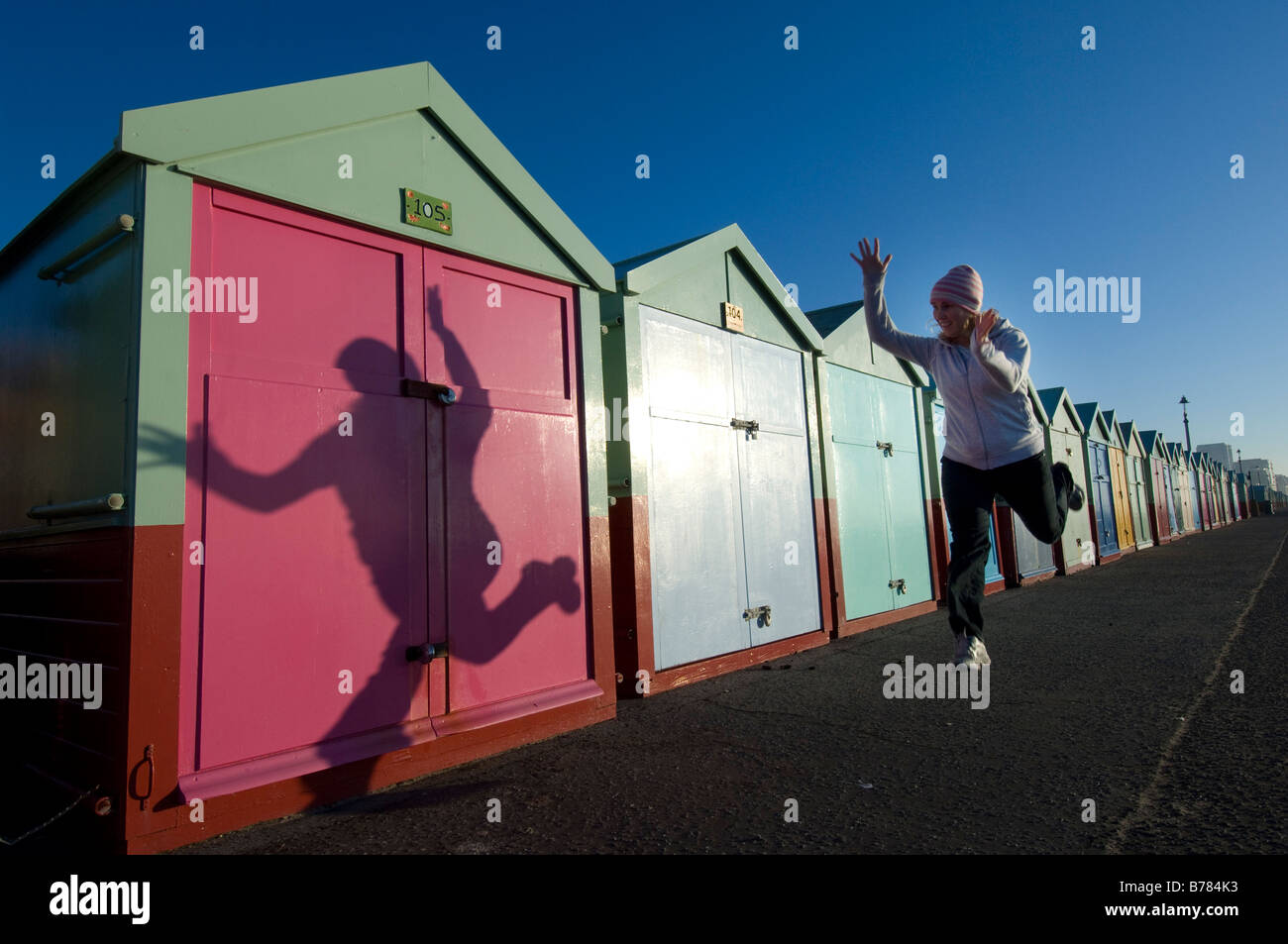Beach Huts on Brighton and Hove seafront with a Jogger casting a shadow as she jumps. Stock Photo