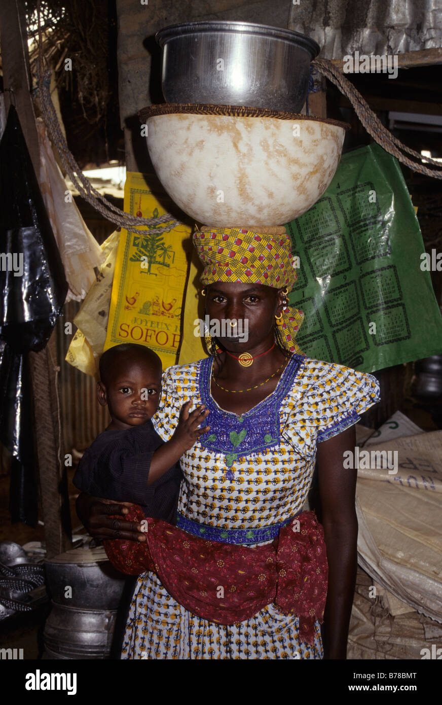 Tortiya, Cote d'Ivoire, Ivory Coast. A Fulani Mother and Child Balancing Calabash and Cooking Pot on her Head. Stock Photo
