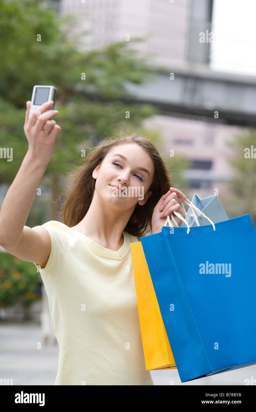 Teenage girl holding shopping bags photographing herself with camera