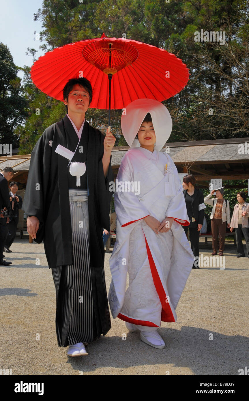 Japanese wedding couple wearing traditional wedding kimonos, bride wearing  a bonnet, groom holding a red parasol in front of th Stock Photo - Alamy