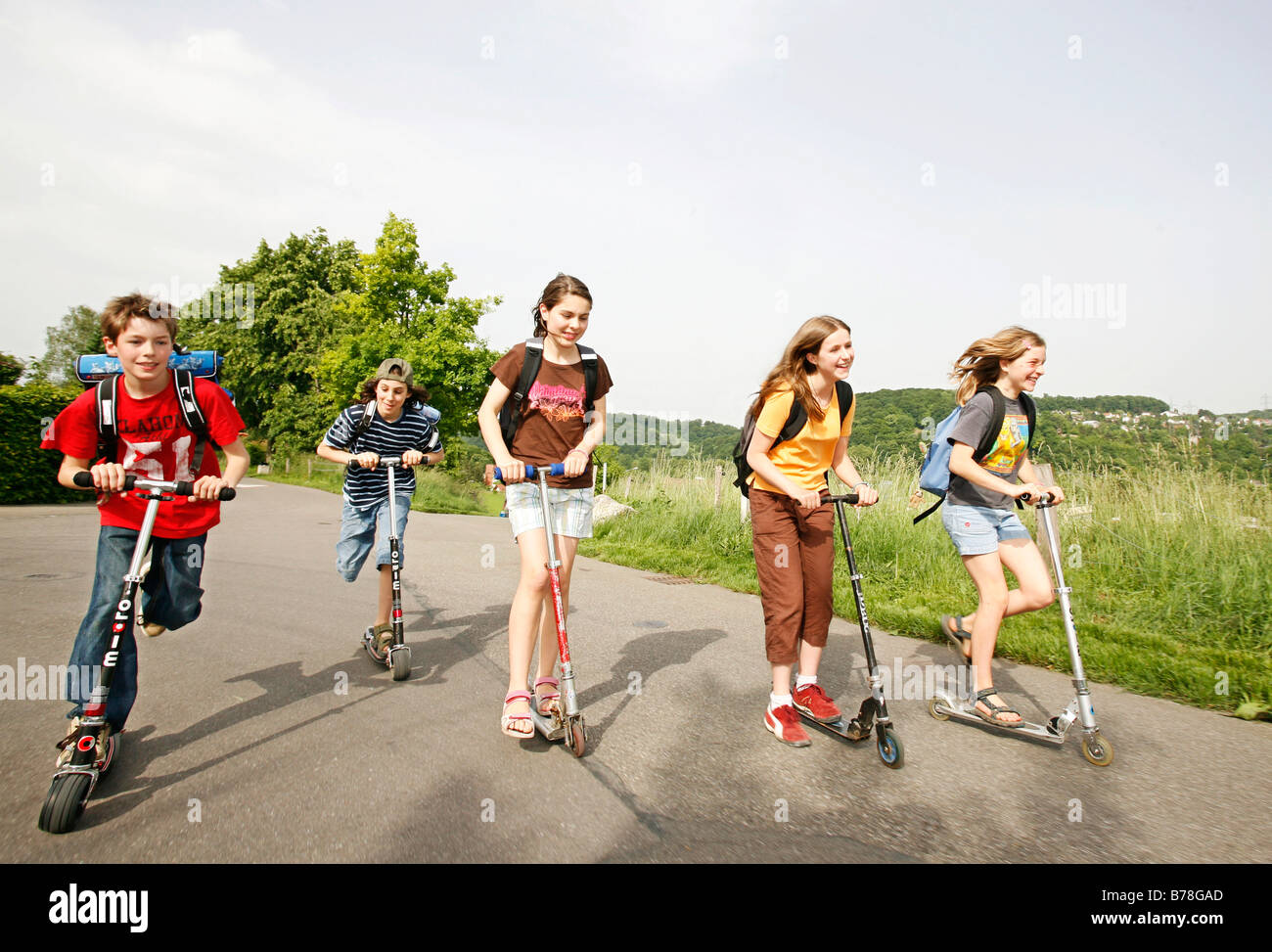 School children, boys and girls, riding kick scooters, push scooters on