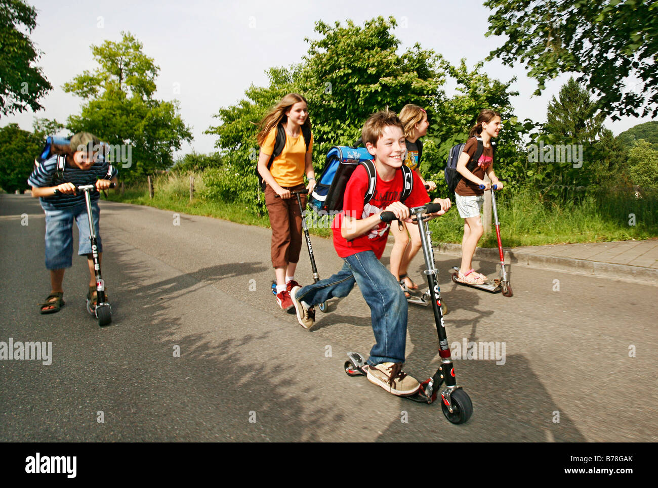 School children, boys and girls, riding kick scooters, push scooters on