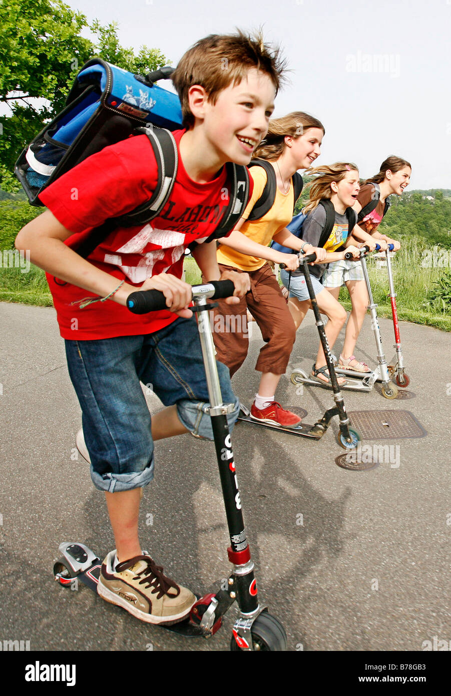 School children, boys and girls, riding kick scooters, push scooters on