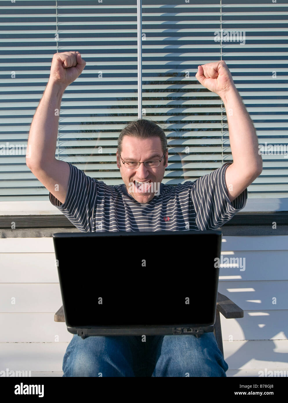 Man sitting on balcony with a laptop, cheering Stock Photo - Alamy