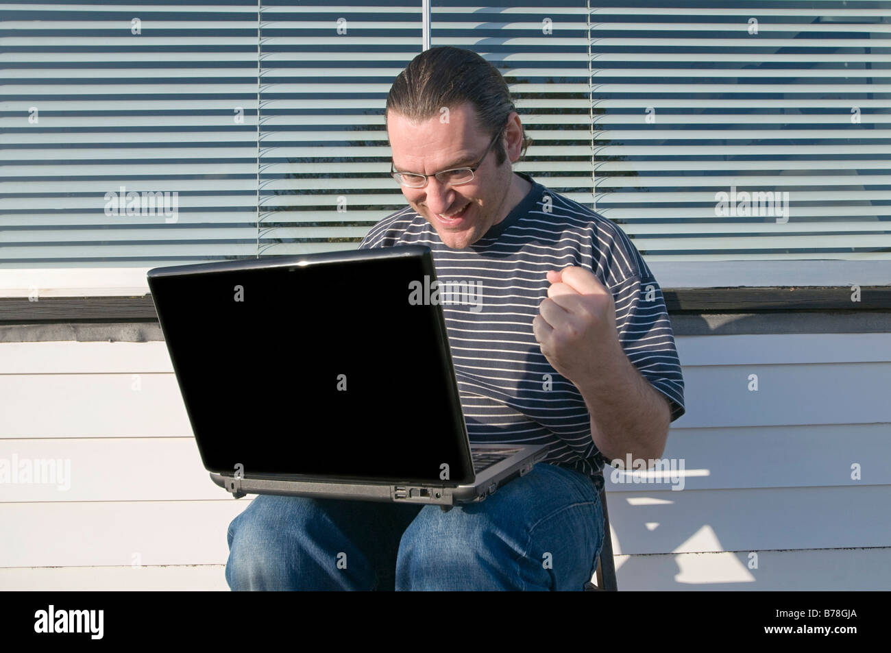 Man sitting on balcony with a laptop, balling his fist Stock Photo
