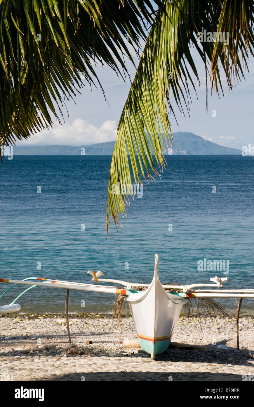 Filipino boat (bangka) on stony beach with palm tree in foreground, Malabrigo, Batangas, Philippines Stock Photo