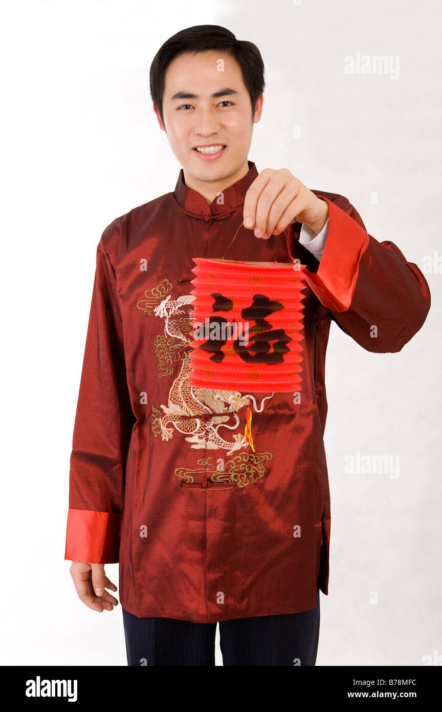 Young man in traditional clothes holding Chinese lantern and smiling at the camera Stock Photo