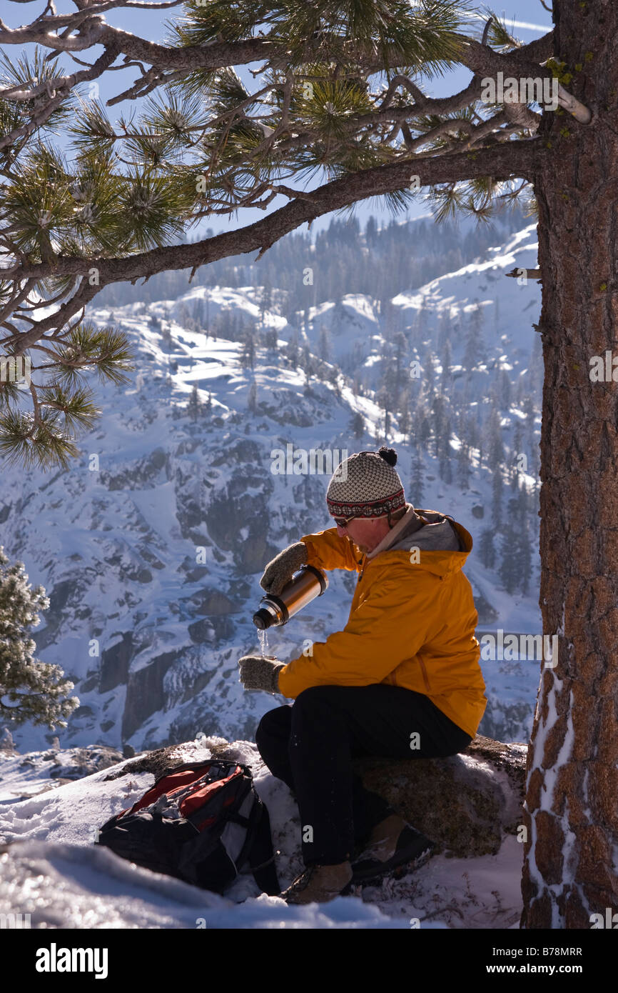 A male hiker pouring a drink from a thermos while hiking in winter on Donner Summit in California Stock Photo