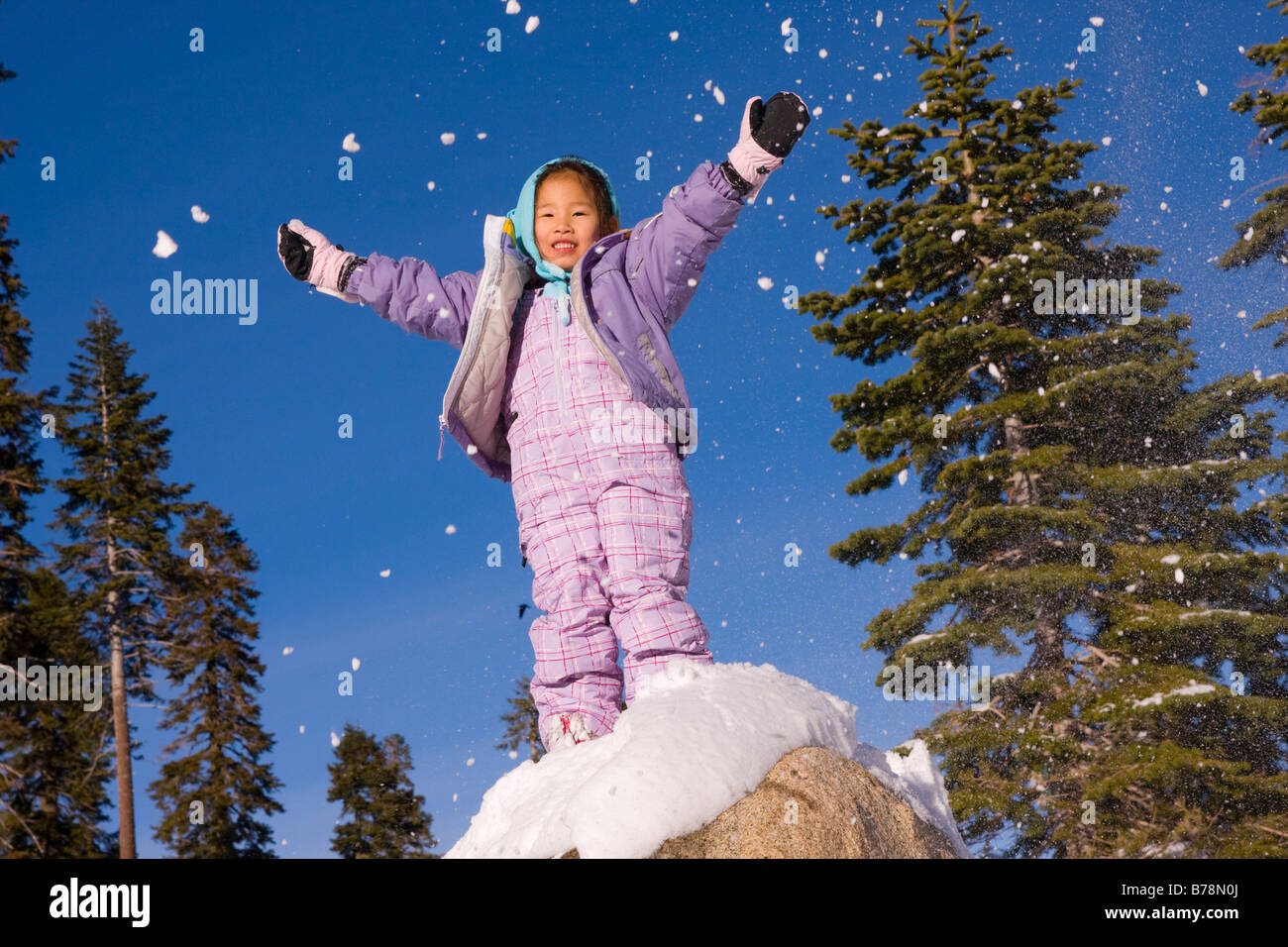 A victorious girl standing on top of a snowy rock at Sierra at Tahoe ski resort near Lake Tahoe in California Stock Photo