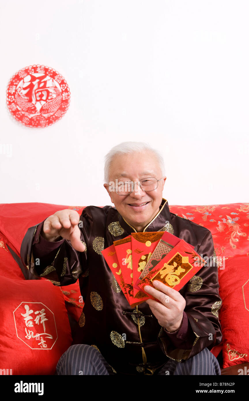 Elderly man in traditional clothes holding red envelopes and smiling at the camera Stock Photo