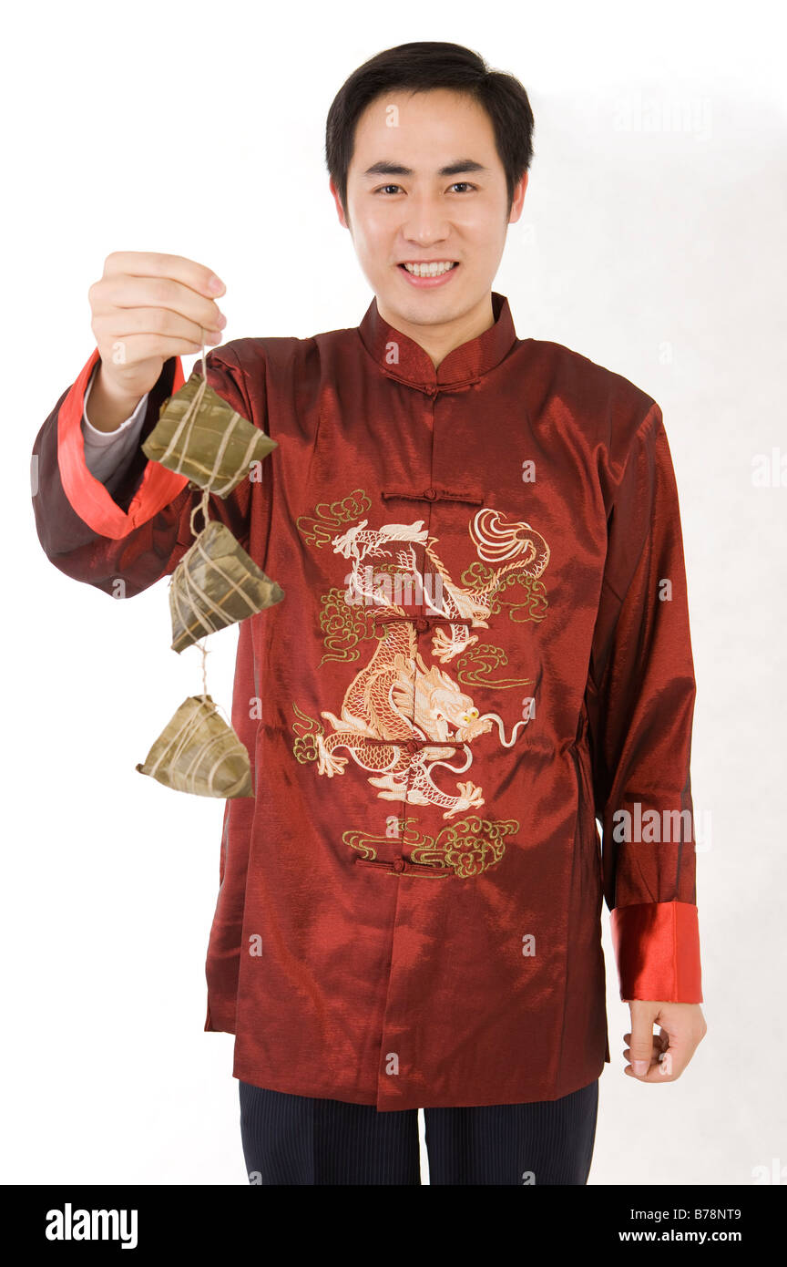 Young man in traditional clothes holding Chinese rice dumplings and smiling at the camera Stock Photo