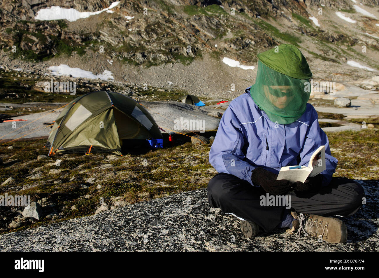 Female hiker with fly net reading book, Ikasartivaq-Fjord, East-Greenland, Greenland Stock Photo