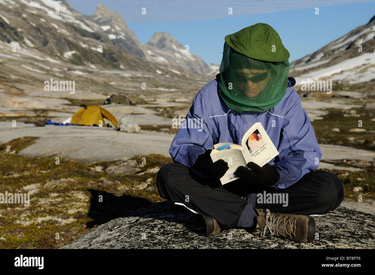 Female hiker with fly net reading book, Ikasartivaq-Fjord, East-Greenland, Greenland Stock Photo