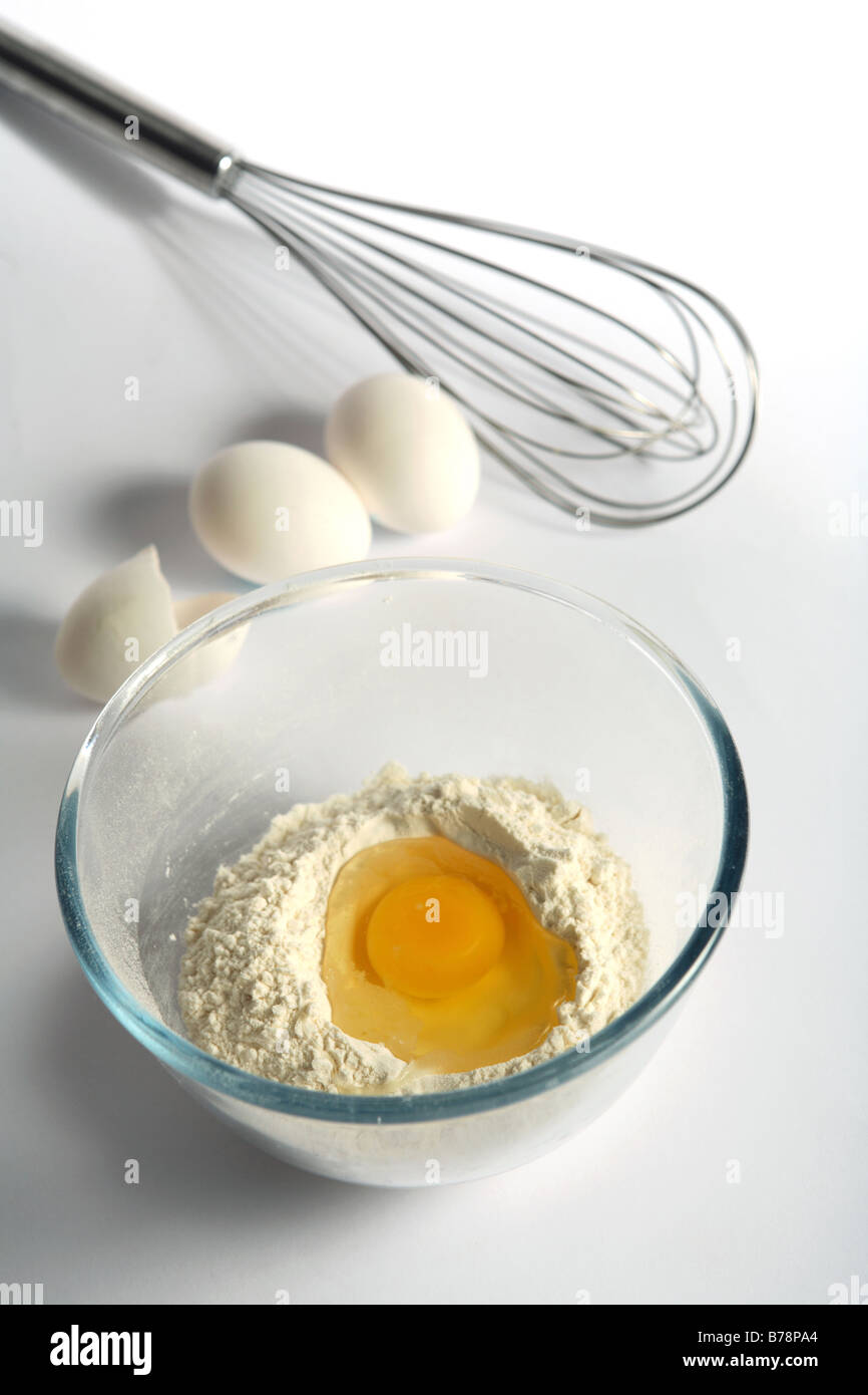 An egg broken into flour in a mixing bowl with other eggs and a whisk