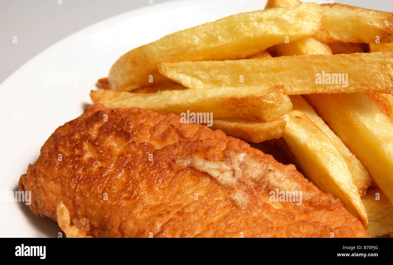 A plate with a piece of battered fish and a pile of British-style chips (French fries). A traditional home-made meal. Stock Photo