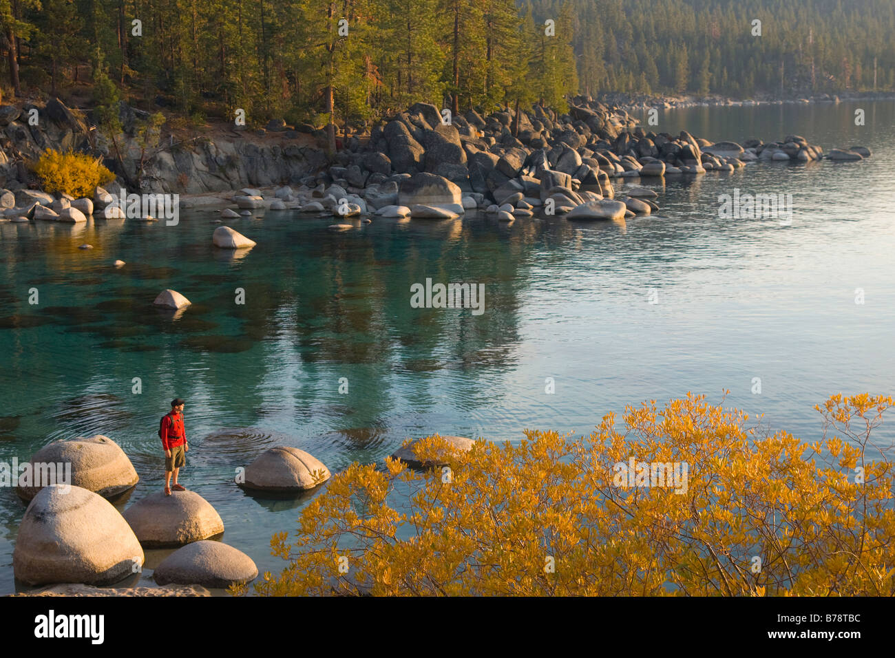 A man standing on a rock on the shore of Lake Tahoe in California at sunset with reflecting water Stock Photo