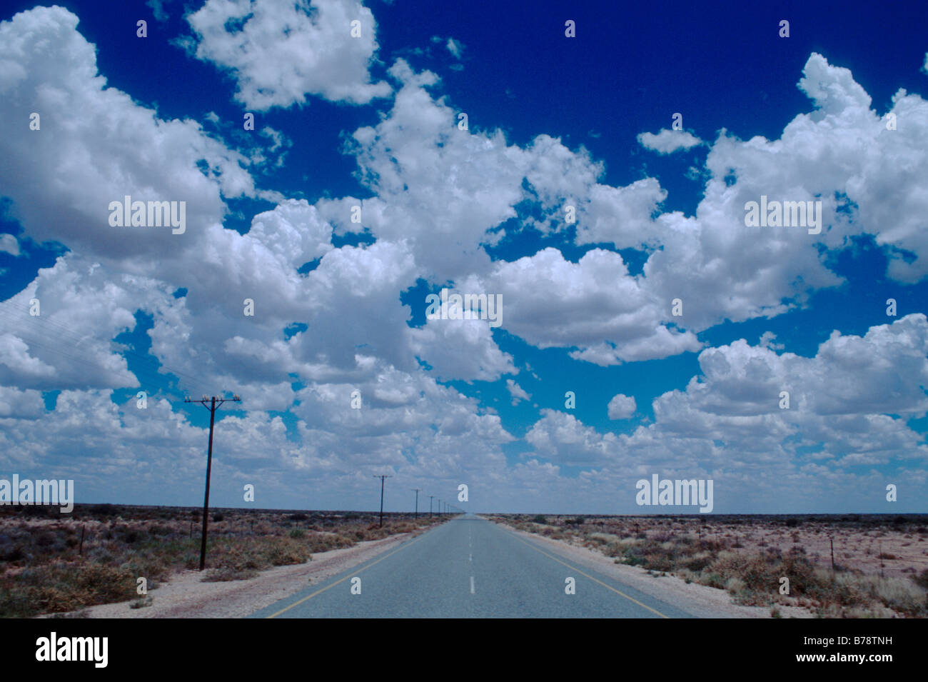 A tar road stretches into the distance with scattered cumulus clouds ...