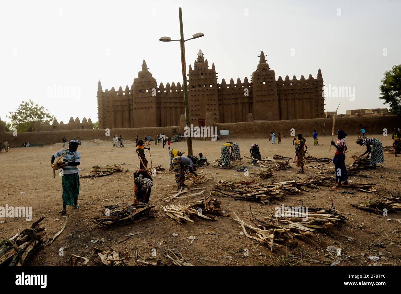 women arranging firewood in front largest mud brick or adobe building in the world, the Great Mosque of Djenné in Mali Stock Photo