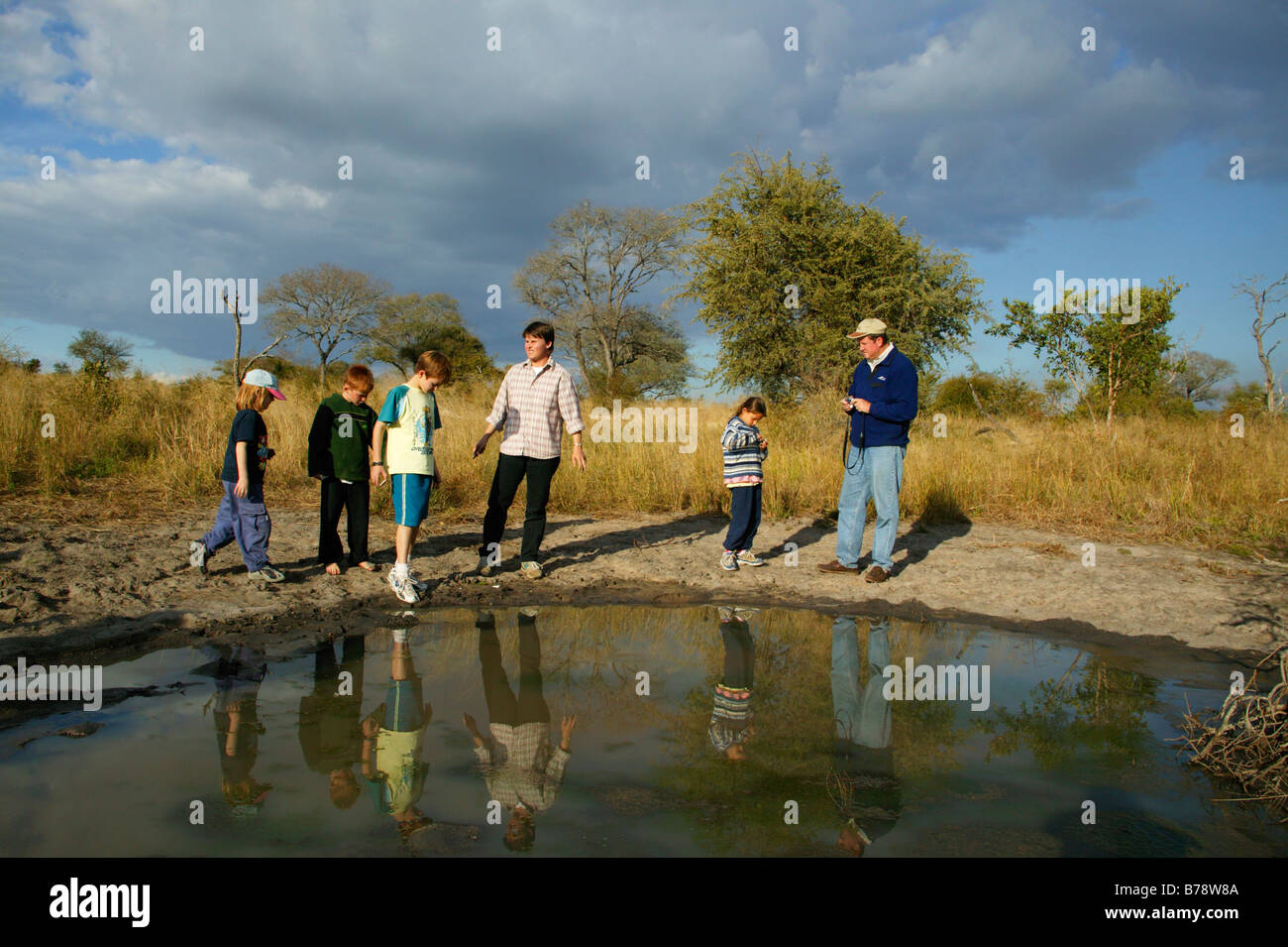 Children looking at animal tracks in the drying mud around a small natural pan in the Bushveld Stock Photo