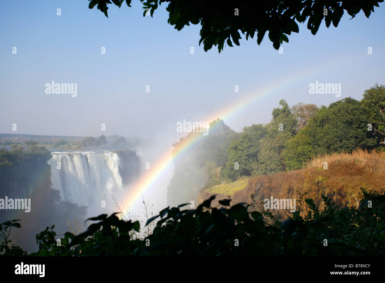 Victoria falls on the Zambezi river with a rainbow and lush rainforest vegetation in the foreground Stock Photo