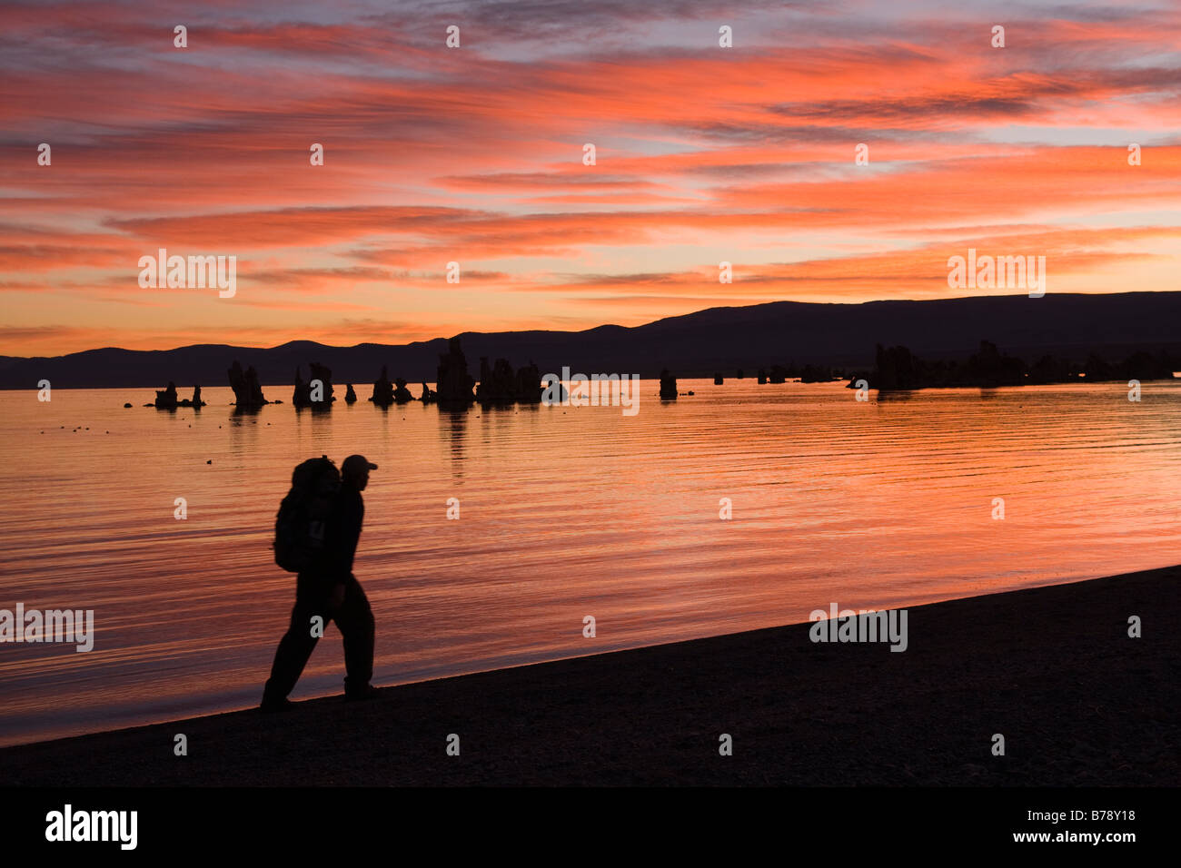 A man hiking along the shore of Mono Lake with reflecting water,tufa towers and clouds in California Stock Photo