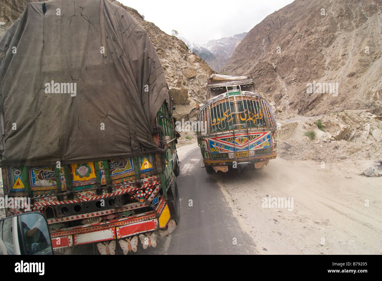 A bus passing an ornate Pakistani cargo transport truck on the one lane Skardu road in Baltistan in Pakistan Stock Photo