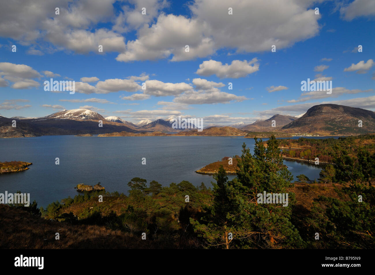 The distant snow capped peaks of Torridon rise beyond the blue waters of Loch Torridon Wester Ross northern Scotland UK Stock Photo