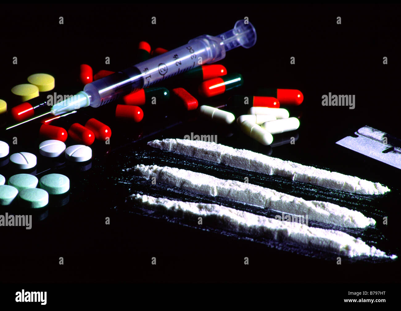 illegal addictive drugs on a glass table including cocaine, pills and a syringe Stock Photo